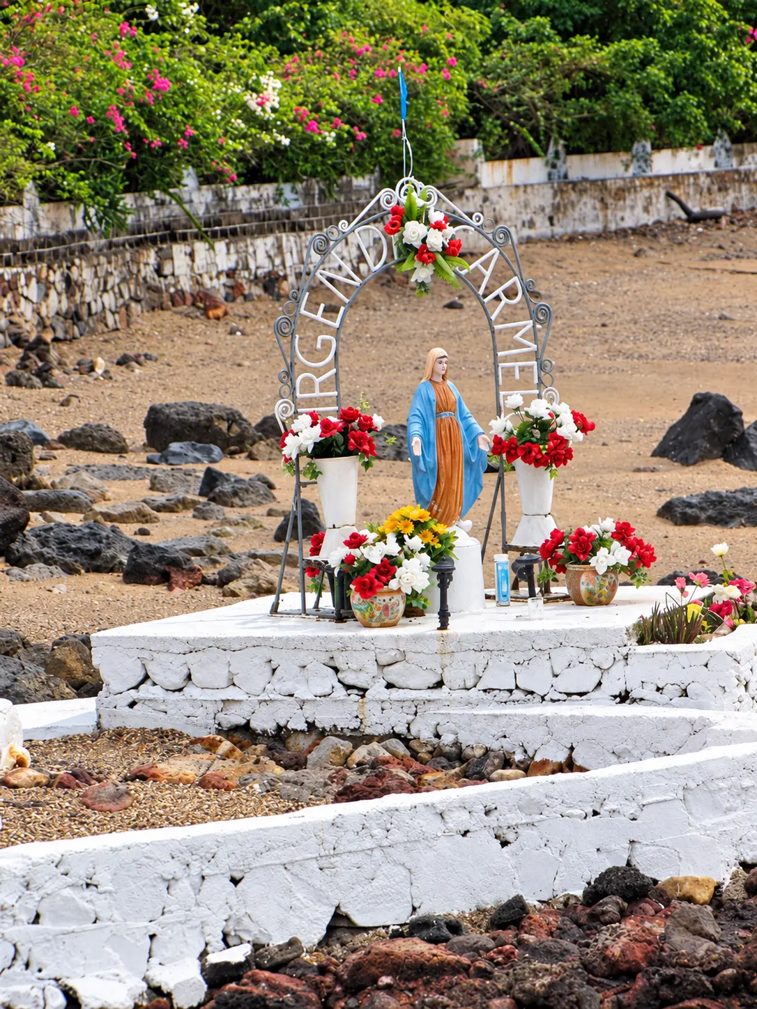 Altar al aire libre de la Virgen del Carmen sobre una base de piedras blancas, rodeado de flores