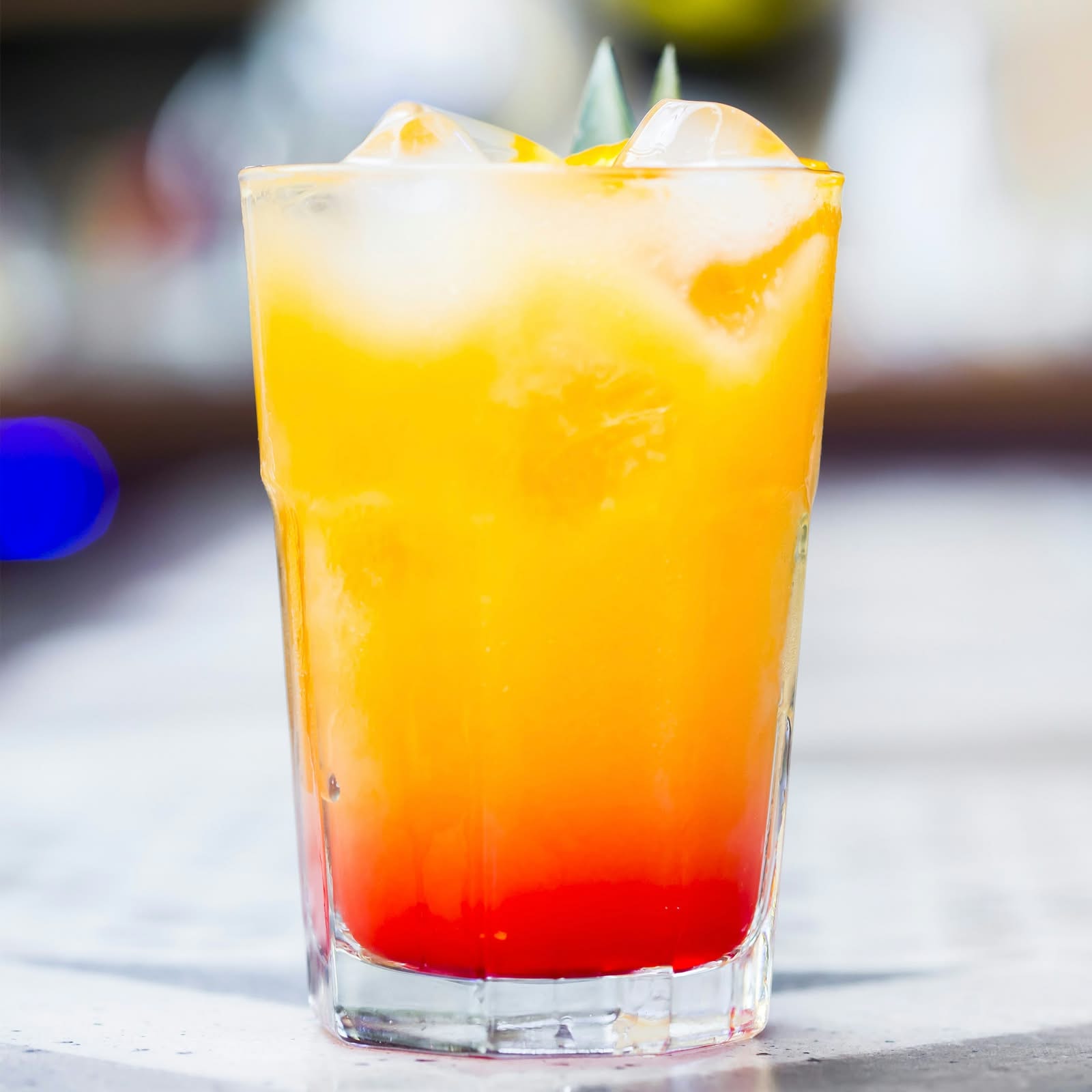 Trago en capas de naranja y rojo con hielo, servido frío en la isla